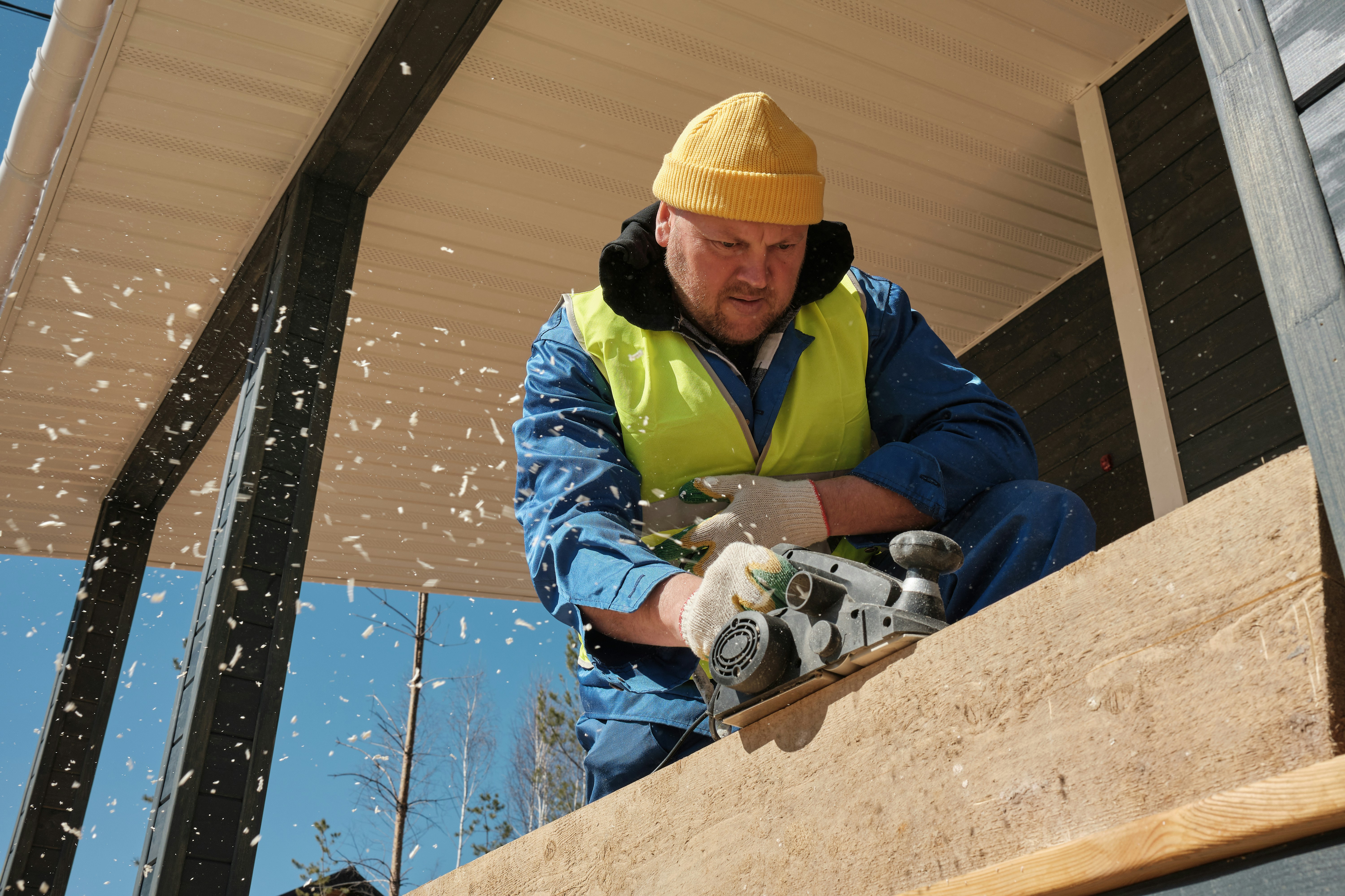 A middle-aged worker runs a sander on a large plank.