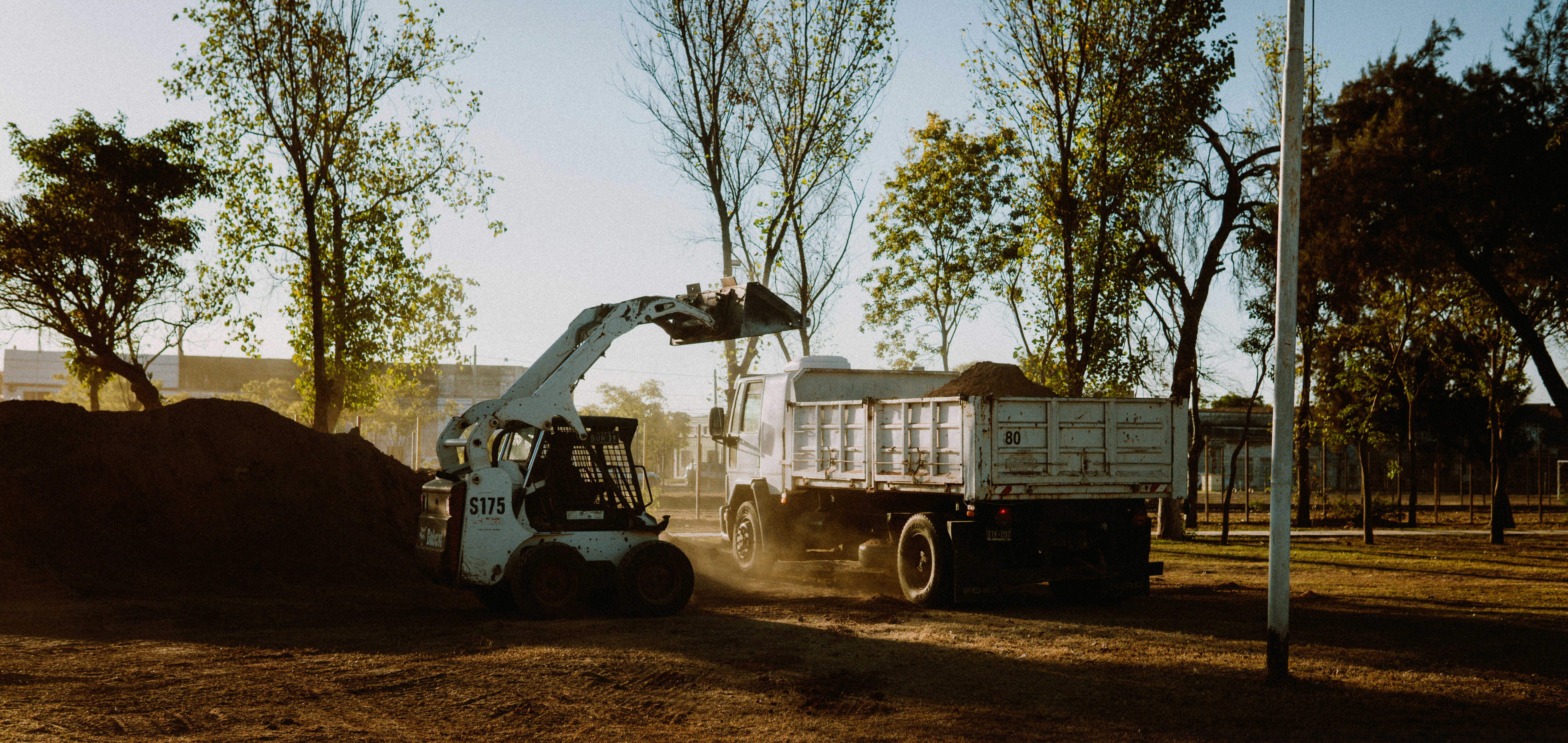 A skid steer loads soil into a dump truck